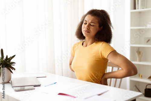 Beautiful Young Black Woman Suffering From Backache While Sitting At Desk At Home, Tired African American Freelancer Lady Having Acute Lower Back Pain After Long Time Working With Laptop Computer