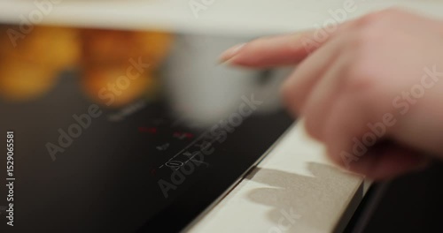 Close up of woman hand presses a button on the electric stove. Modern technology.