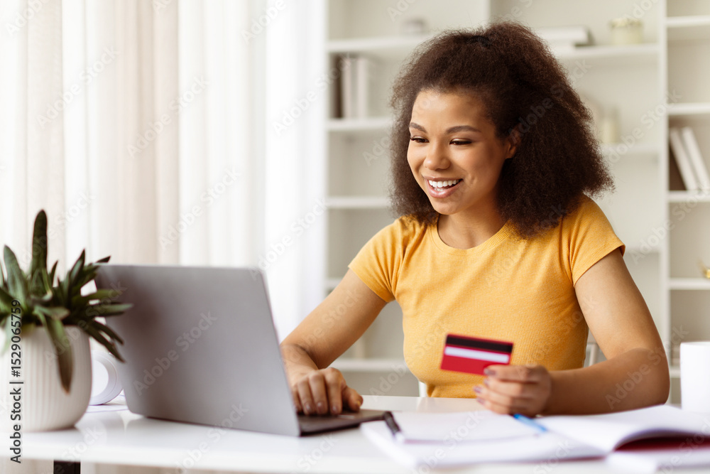 Young African American woman shopping online at home, holding credit card while using laptop at her desk, smiling black female browsing internet banking, making online transaction Young African American woman shopping online at home, holding credit card while using laptop at her desk, smiling black female browsing internet banking, making online transaction