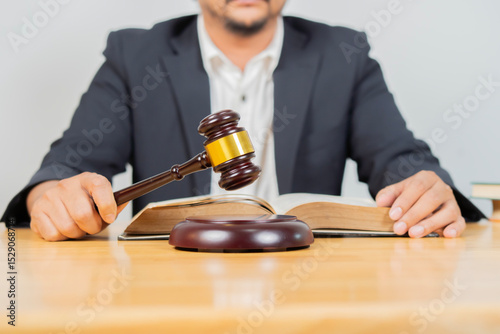 A lawyer with a gavel in hand and a book on the table in front of him in an office setting