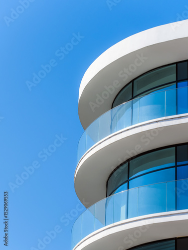 Modern curved glass balconies on a white building against clear blue sky. Minimalist architectural design.