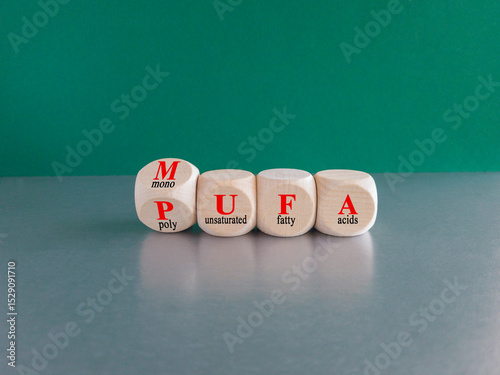 Cubes form the acronym MUFA (Monounsaturated Fatty Acids) and PUFA (Polyunsaturated Fatty Acids). Beautiful green background, grey table. Business and medical concept.