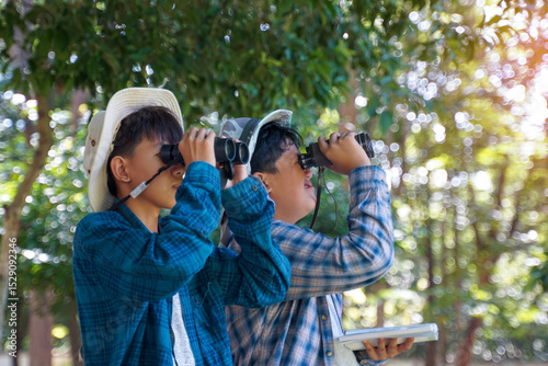 Two Asian boys use binoculars to study the local birds at school. Soft and selective focus.