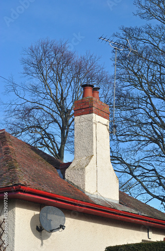 Satellite Dish and Chimney on Old Building with Leafless Trees and Blue Sky 