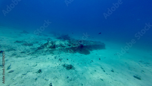 The hull of a sunken boat underwater. The overturned remains of a boat on a sandy sea bottom. A sunken boat on a deserted sea bottom in clear transparent water.