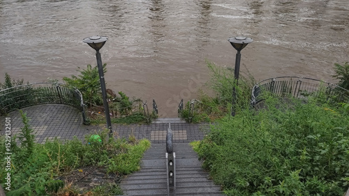 muddy waters of the vltava river flooding the embankment stairs and surrounding vegetation in prague after heavy autumn rainfall