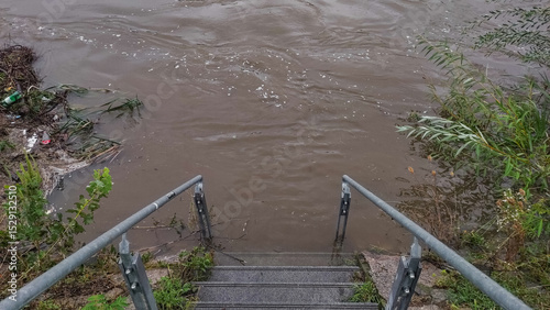 muddy water from the vltava river is covering stairs leading to the river after heavy rainfall in prague, with debris and plants floating on the surface