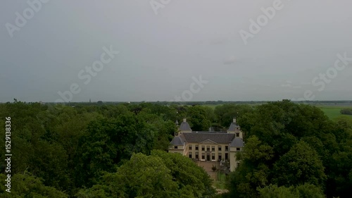 Aerial view of a historic castle surrounded by a forest, with vast green fields, winding waterways, and a river stretching across the flat Dutch countryside under a partly cloudy sky.