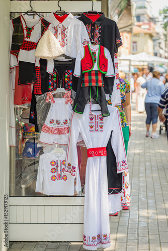 Traditional national Bulgarian folk costumes for kids and adults displayed outside local shop. Concept of cultural heritage, cultural fashion, cultural preservation