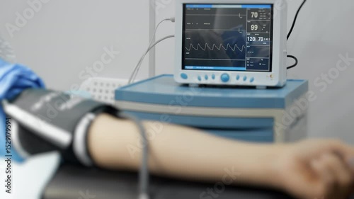 Close-up of patient's hand in operating room with blood pressure monitor on hand and heart rate monitor in background. Modern medical surgical equipment in clinic.