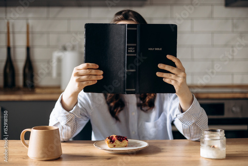 Young woman reading her Bible while having breakfast in a cozy home kitchen.