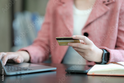 E-commerce and online banking. Close-up of a young female internet store customer, an e-bank client, making a payment from a home computer, holding a prepaid credit card in her hand.