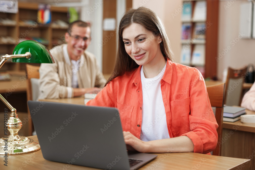 Fototapeta premium People studying at desks in public library, selective focus