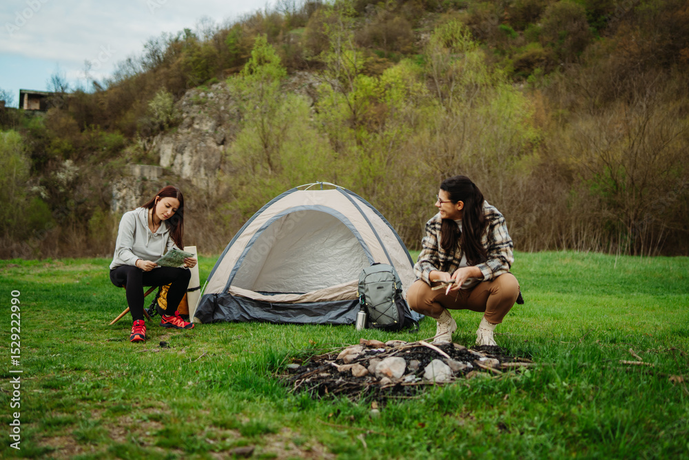 Fototapeta premium Two female friends setting up camp in the forest after hiking or trekking 