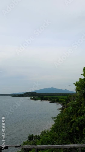 a calm sea view with agricultural rice fields and a backdrop of cloud-covered mountains.