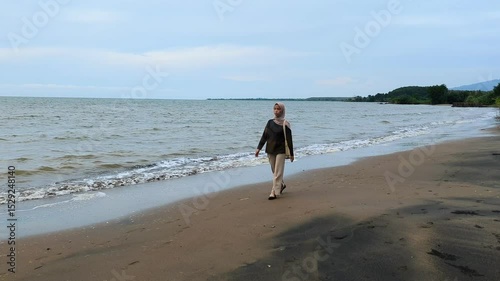 Javanese women wearing hijab walking on the beach, Asian Muslim women walking on the beach with small waves crashing and empty sky for advertising space.