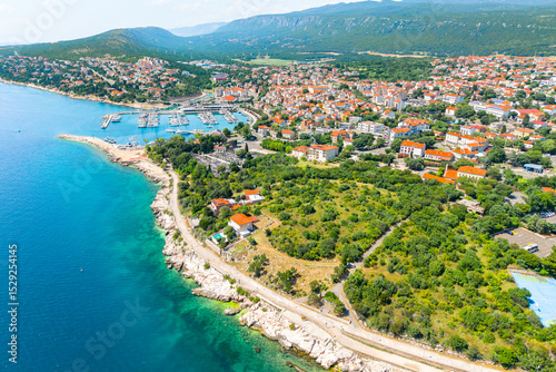 Fototapeta Naklejka Na Ścianę i Meble -  Stunning aerial panorama of Novi Vinodolski, showing the coastal town with red-roofed houses, marina, rocky beaches, and lush green hills surrounding the blue Adriatic Sea
