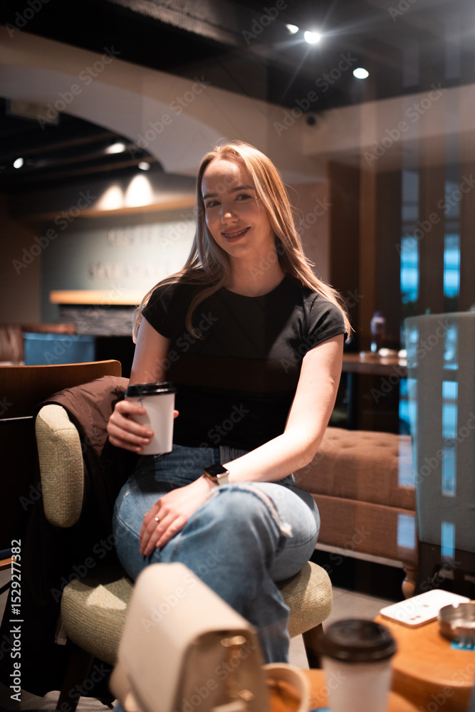 Obraz premium Young woman smiling and drinking coffee in cozy cafe