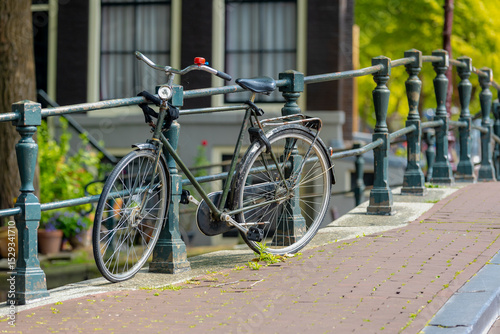 Selective focus of old classic vintage bicycle parked on Amsterdam canal bridge with blurred traditional houses, Cycling is a common mode of transport in Holland, Netherlands land of bicycles.