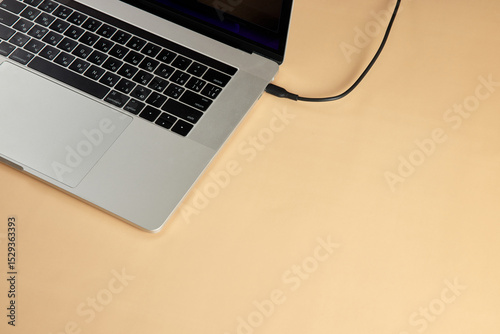 cable plugged in laptop on beige background, close-up. Charging battery laptop, copy space