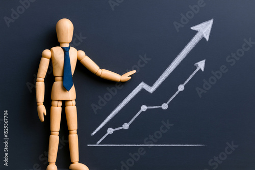 Wooden mannequin dressed in business suit and tie stands next to rising graph drawn with chalk on dark background, symbolizing growth and strategy in business