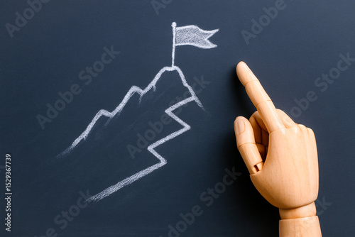 Wooden hand pointing at chalk drawing of mountain with flag at summit, symbolizing achievement and success, emphasizing importance of business strategy in reaching goals