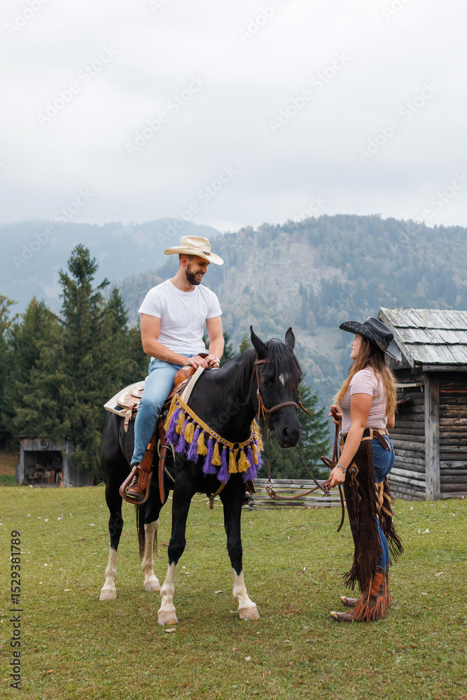 Obraz premium Cowgirl instructor, holding the reins, watching and helping a young rider mount his horse at the ranch riding school