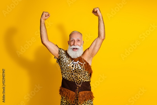 Photo of excited old man in caveman costume raise fists up winning wear animal fur isolated yellow color background