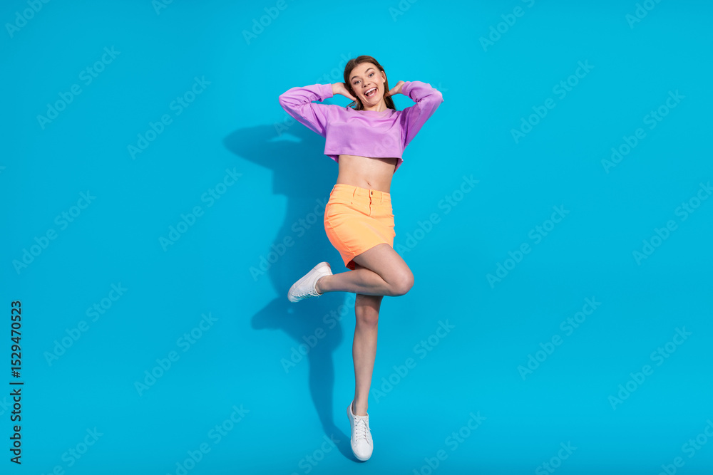 Obraz premium Cheerful young woman in vibrant outfit posing against a blue background with playful gesture and joyful expression