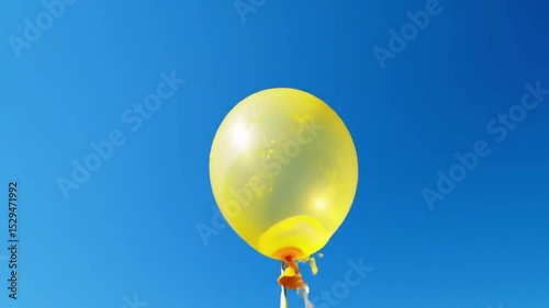 Bright yellow water balloon tied up and floating in air with deep blue sky background — perfect for summer themes, playfulness, or balloon product visuals.

 photo
