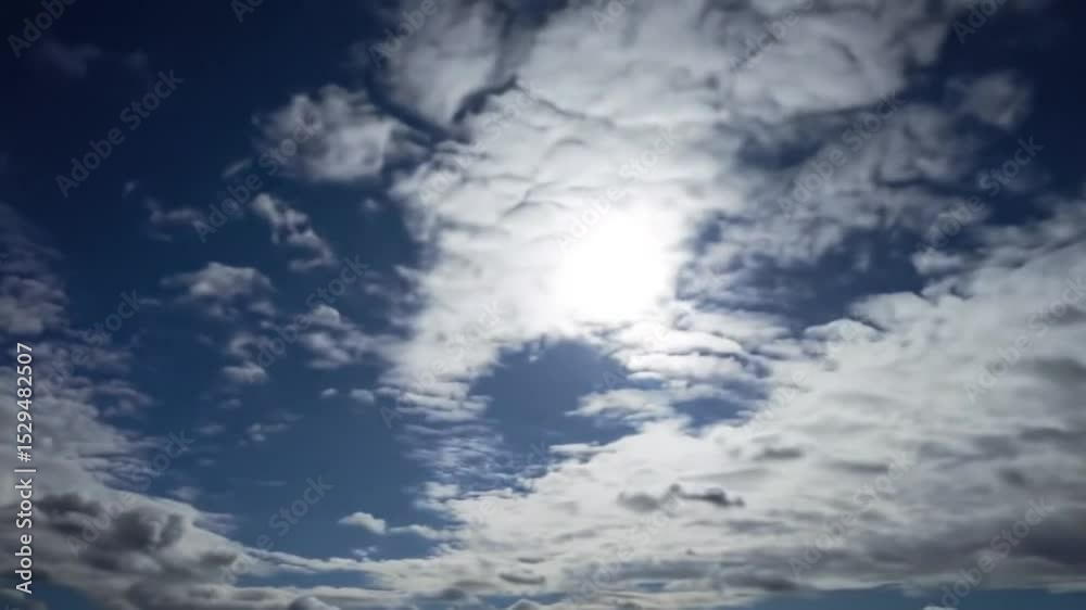 Sunlight shining through a sky filled with fluffy white clouds and patches of blue sky visible