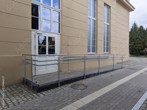 Wheelchair-accessible entrance ramp with metal handrails outside a public building, promoting inclusive infrastructure and accessibility.