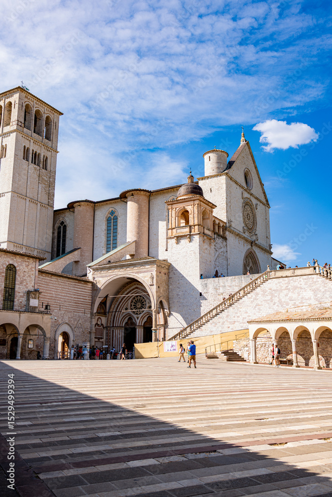 Fototapeta premium Tourists walk near the Basilica of Saint Francis in Assisi, Italy, a UNESCO World Heritage Site and a major pilgrimage destination