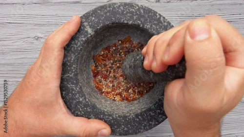 Top view of the hand with heavy pestle grinding mix of spices and peppers in the grey stone mortar
