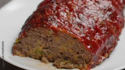 A sharp knife cuts a piece of freshly baked meatloaf. Hot steam rises from the juicy and savory slice being lifted. A classic homemade comfort food dinner is ready to be served and enjoyed