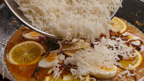 Steamed basmati rice is poured into a pan with simmering beef in a rich creamy sauce. The process of making a traditional and delicious homemade biryani dish. A closeup of culinary preparation