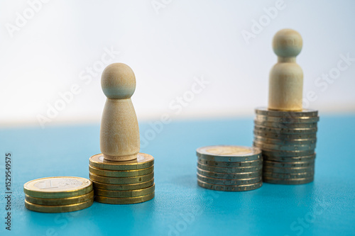 Concept of unequal pay in the workplace between men and women. Wooden figures on piles of coins.