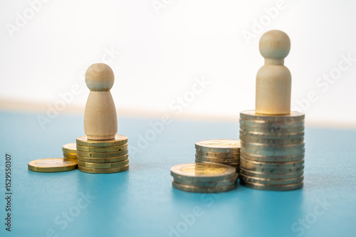 Concept of unequal pay in the workplace between men and women. Wooden figures on piles of coins.
