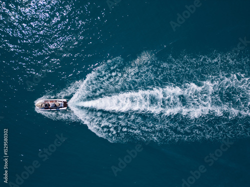 Aerial view of a jet ski speeding across dark blue water, leaving a dynamic white trail. Captured by drone from above, showcasing motion, power, and summer fun on the sea