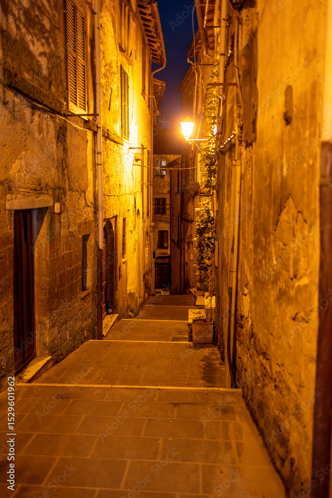 Obraz premium A nighttime view of Pitigliano, a charming Tuscan village perched on cliffs, glowing with warm lights and rich in medieval atmosphere