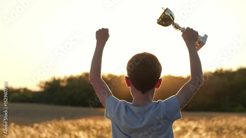 Child raises trophy cup at sunset, family celebrating success. Child stands proud with trophy raised high, symbolizing child achievement, proud family moment. Child represents growth, support family.