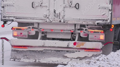A truck is parked on the road in winter with its hazard lights on.