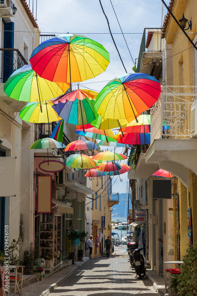 Fototapeta premium Colorful Umbrellas Adorning Aegina Greece Alley with Quaint Shops