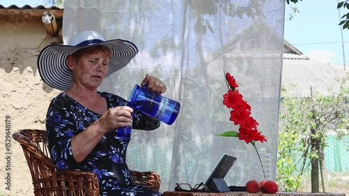 An elderly woman talks and drinks water in the garden.