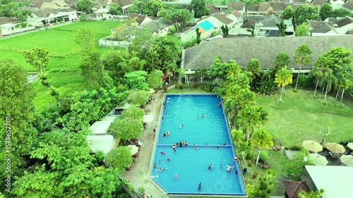 Overhead shot of a blue swimming pool surrounded by lush greenery and buildings