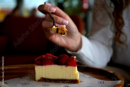 Young woman enjoying a slice of strawberry cheesecake. A delightful moment of indulgence, sweetness, and joy, capturing the pleasure of dessert in a cozy, relaxed atmosphere.

