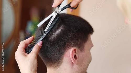 A young woman hairdresser thins a man's hair.