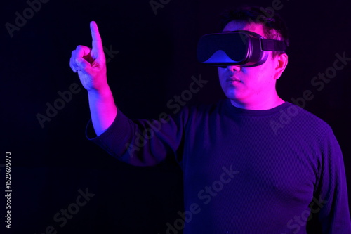 A person wearing a VR headset, pointing upwards with one finger as if interacting with a virtual screen, bathed in vibrant blue and pink neon light on a dark background.