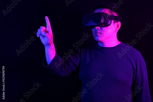 A person wearing a VR headset, pointing upwards with one finger as if interacting with a virtual screen, bathed in vibrant blue and pink neon light on a dark background.