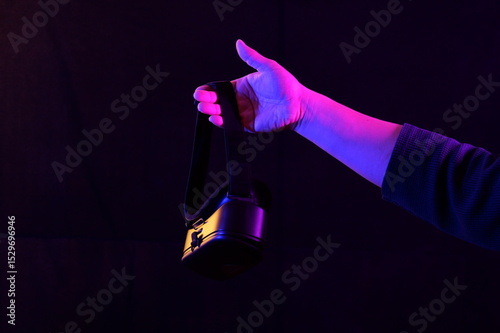 A person wearing a VR headset, with hands raised as if interacting with a virtual environment, illuminated by blue and pink neon lights against a dark background
